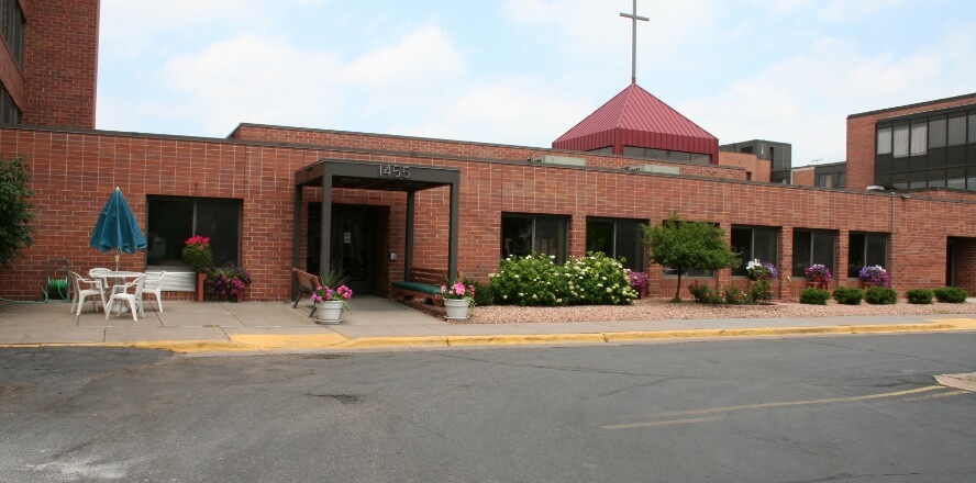 Exterior view of the Como Park senior living campus with a brick building, entrance canopy, and a red-roofed chapel.