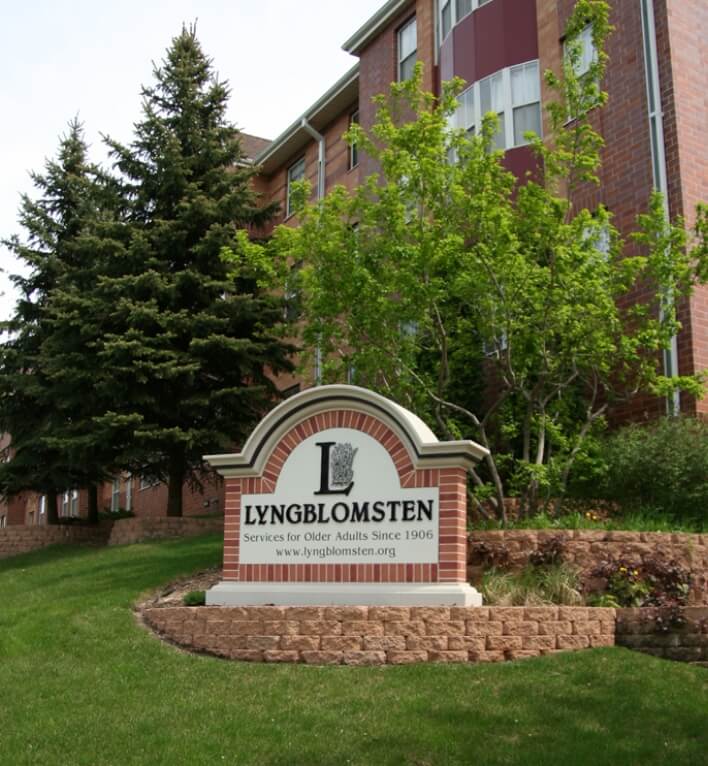 A Lyngblomsten sign in front of a red-brick building with green trees in the background.