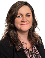Professional headshot of Cosmina Strain, a woman with wavy brown hair wearing a black blazer and patterned blouse, smiling at the camera.