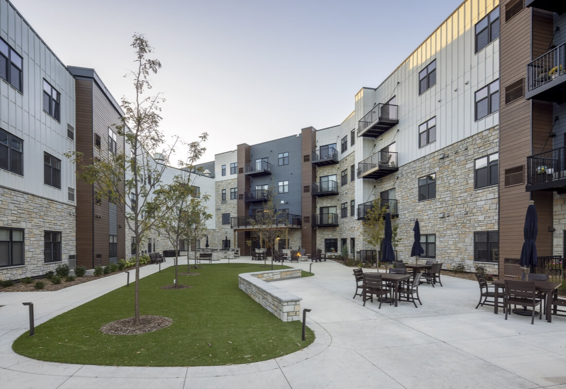 Courtyard with tables, trees, and walking paths surrounded by apartments
