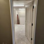 A partially open white door leading to a room under construction, featuring a red ladder and white panel inside. The floor is covered in construction dust.