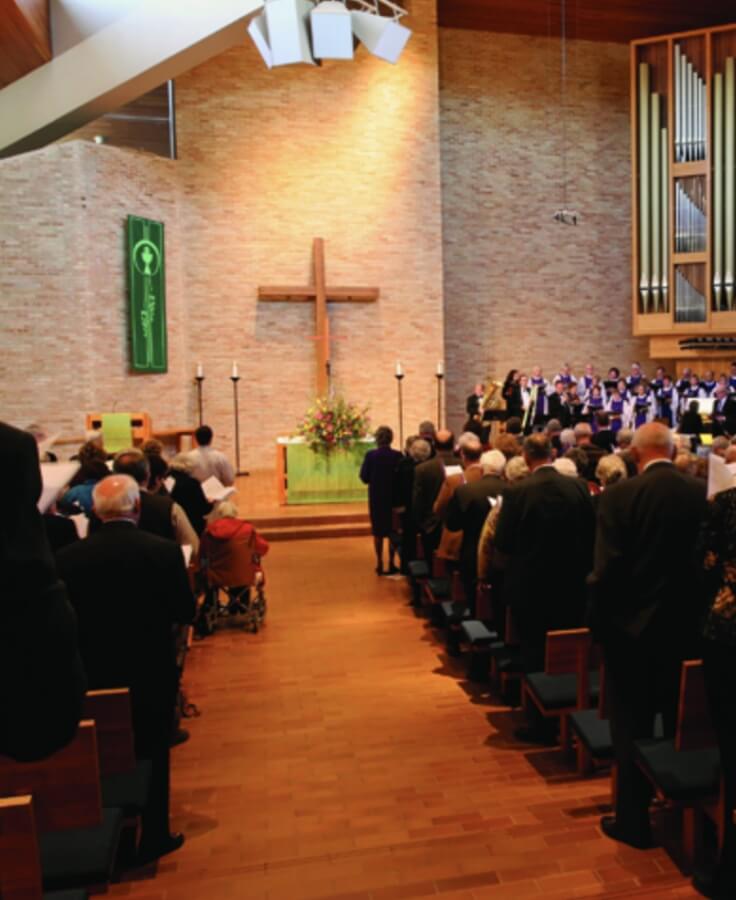 Congregation attending a church service at Lyngblomsten's 100-year anniversary, featuring a choir and a large wooden cross.