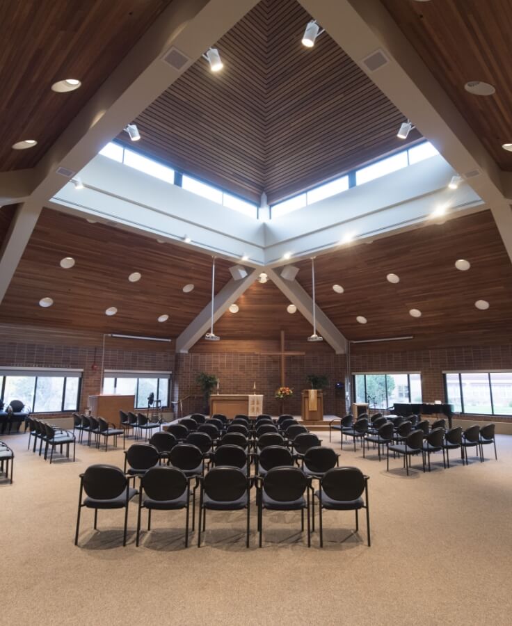 Interior view of the Lyngblomsten chapel with wooden ceilings, a central cross, and rows of chairs arranged for a service.