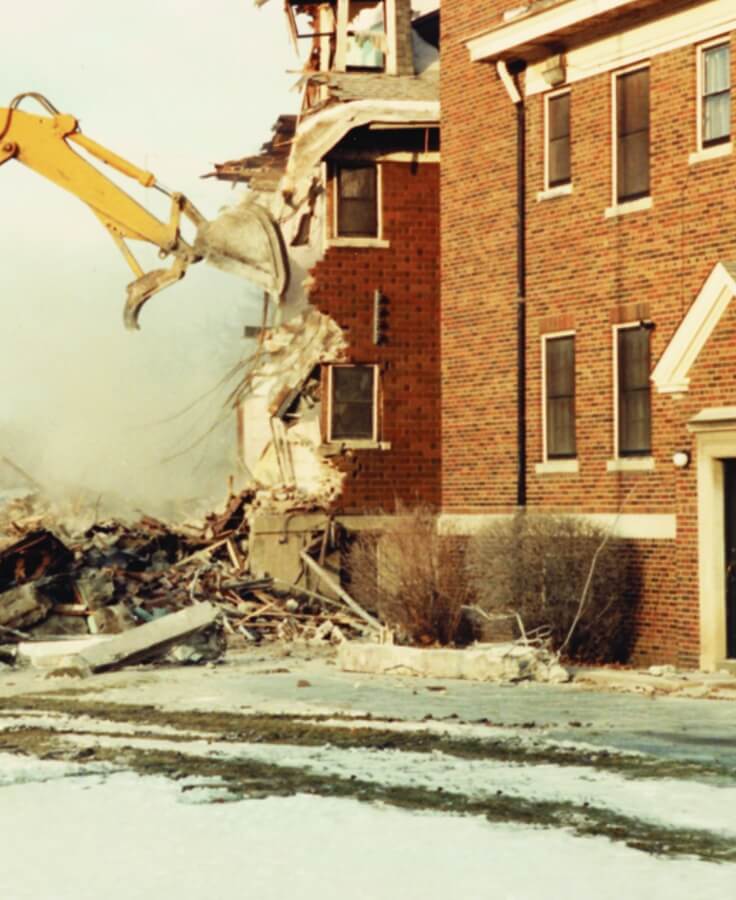 Demolition of the original Lyngblomsten building in 1933, showing a construction excavator tearing down a brick structure.
