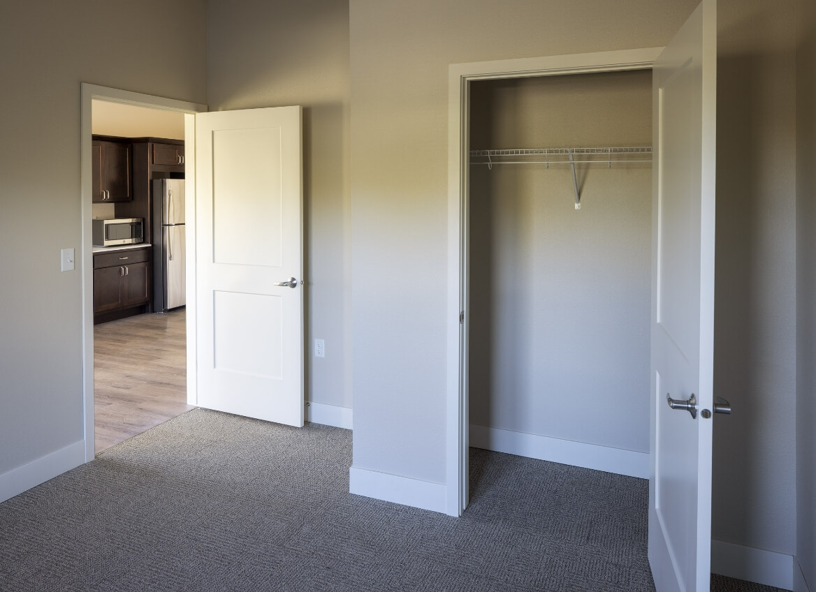 Memory Care bedroom with open closet and view into kitchenette