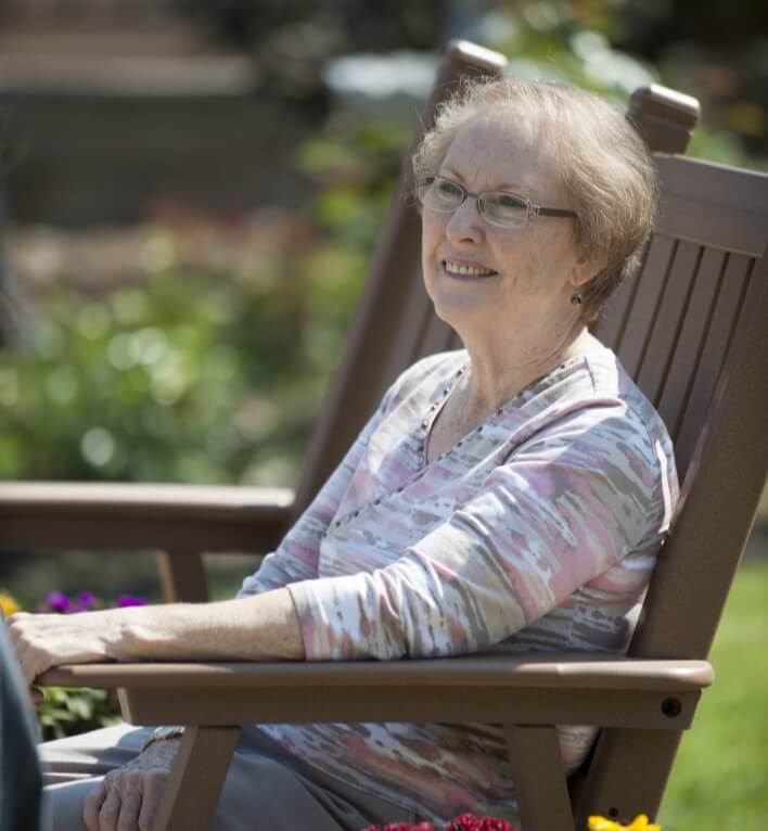 Older woman sitting and smiling in a rocking chair outdoors