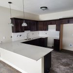 A newly renovated kitchen in a senior living apartment at Lino Lakes, featuring dark wood cabinets, a white quartz countertop, and modern pendant lighting.