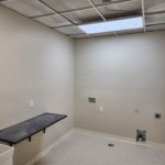A utility room under renovation with a black floating shelf, exposed ceiling panels, and unfinished wall outlets.