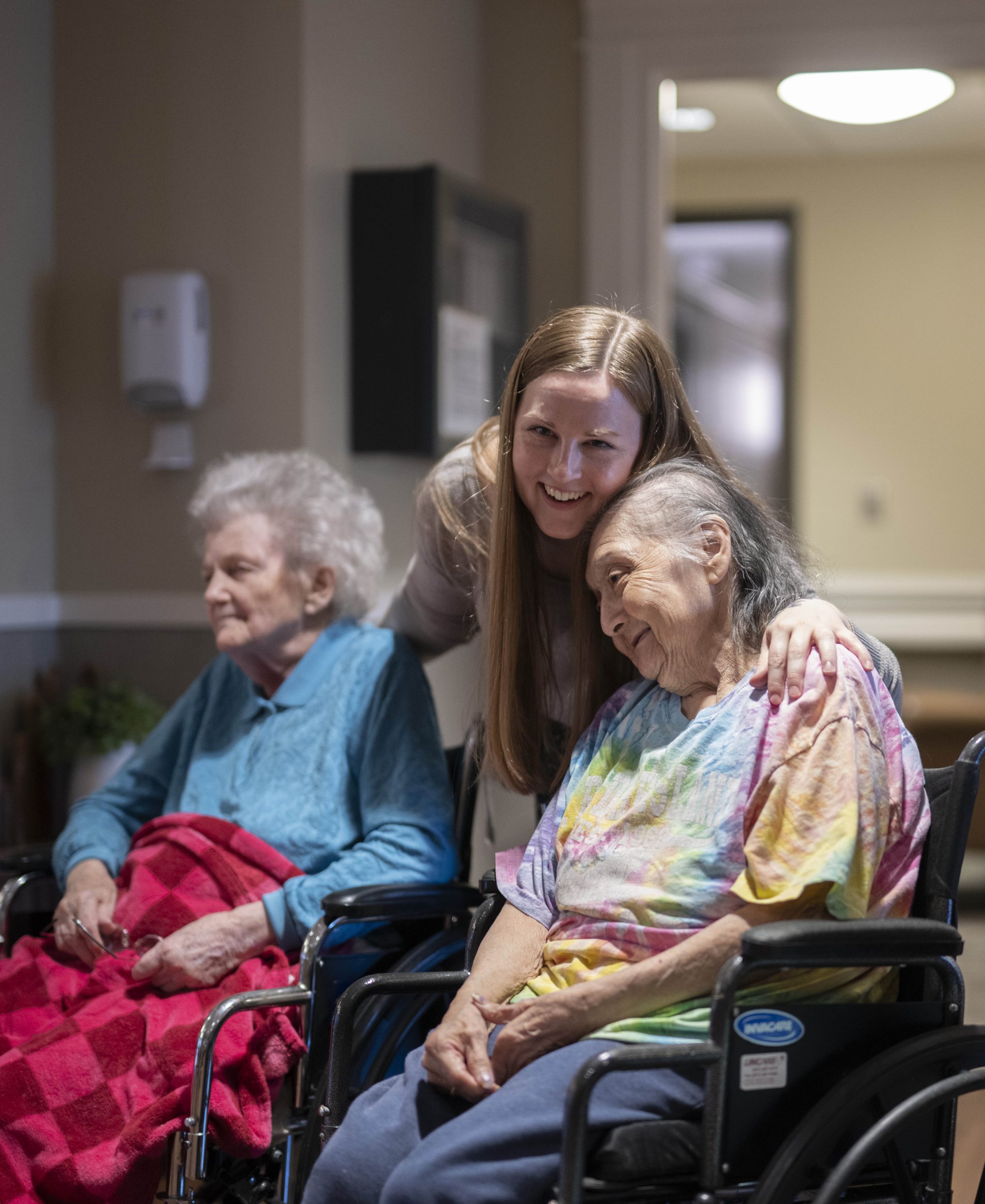 A therapeutic recreation coordinator embraces two residents of the care center while smiling for the camera.