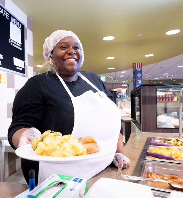 An employee hands staff, guests, and residents today's hot menu items from behind the counter.