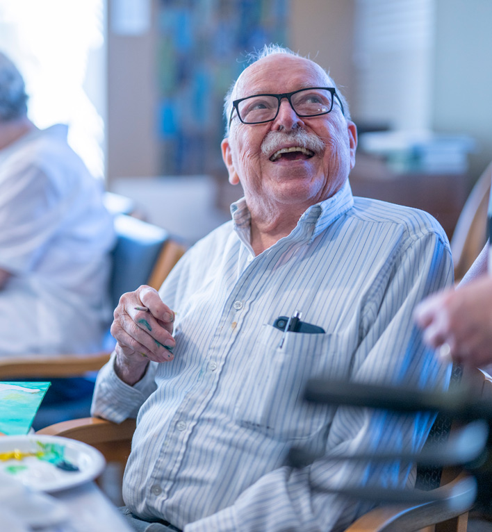 A resident participating in Art with Heart smiles at the instructor as they work on a project.
