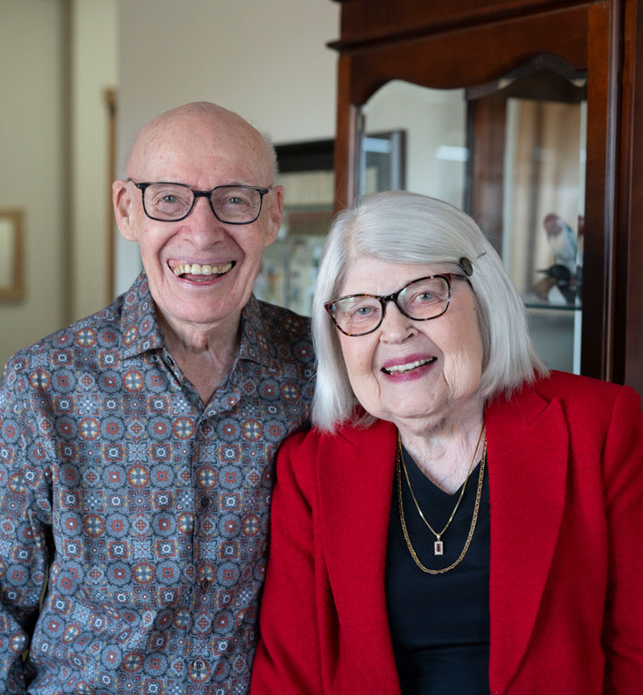A couple from The Heritage at Lyngblomsten smile for a photo in their living room.