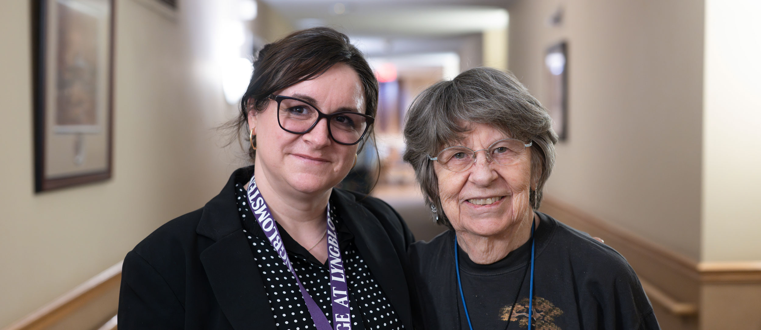Executive Director of The Heritage at Lyngblomsten poses for a photo with a resident in the hallway.