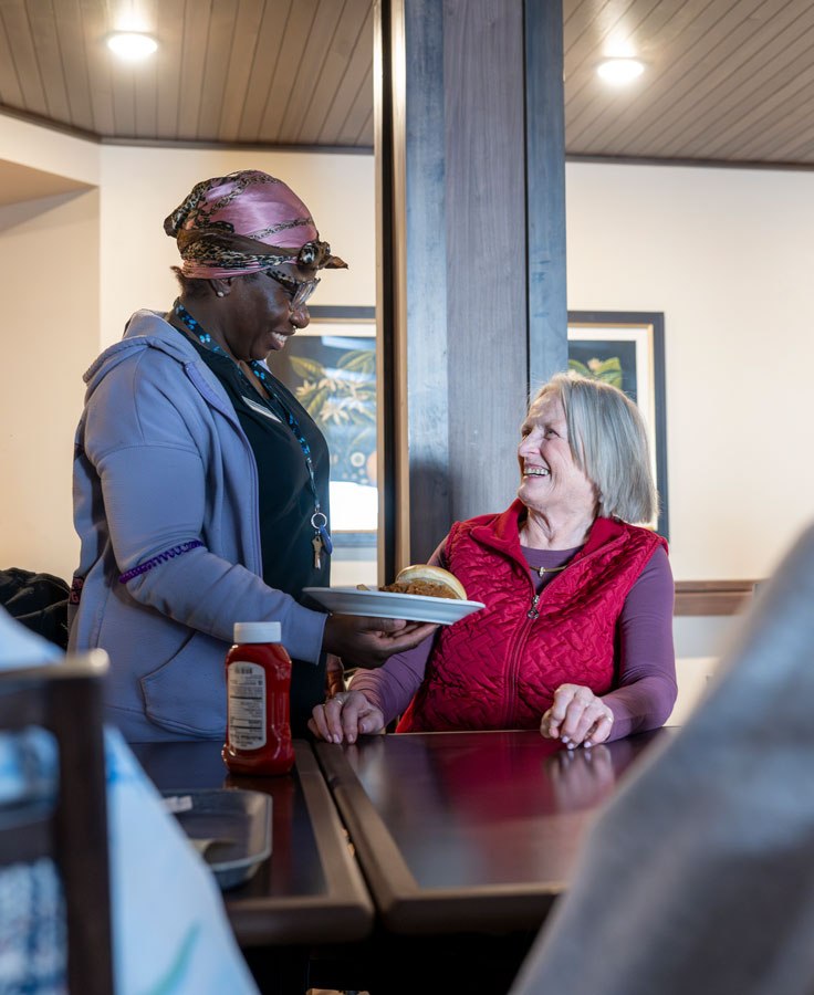 Assisted Living staff member hands a resident food (prepared fresh in our kitchen) in the common dining room.