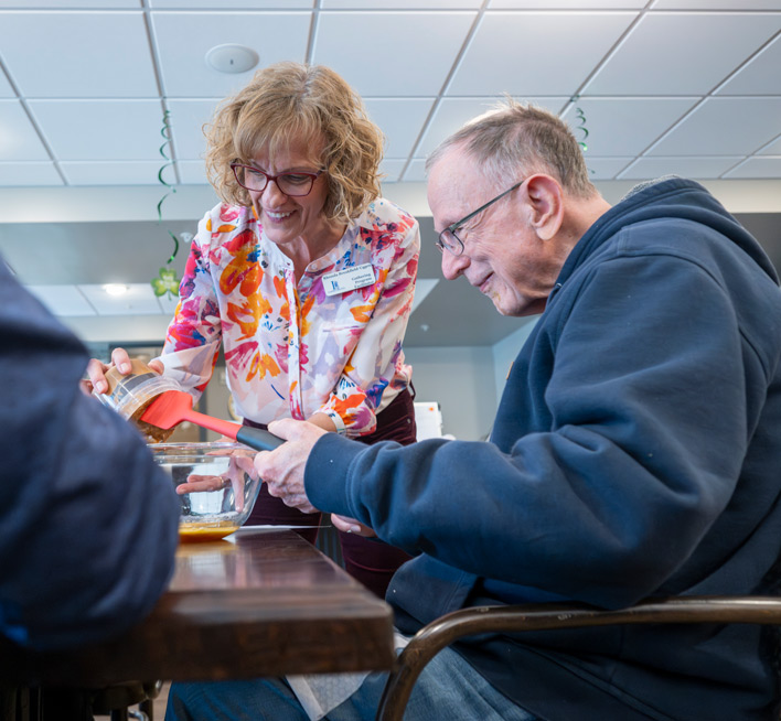 One of the Program Coordinators of The Gathering, helps a participant scrape out an ingredient while baking a sweet treat.