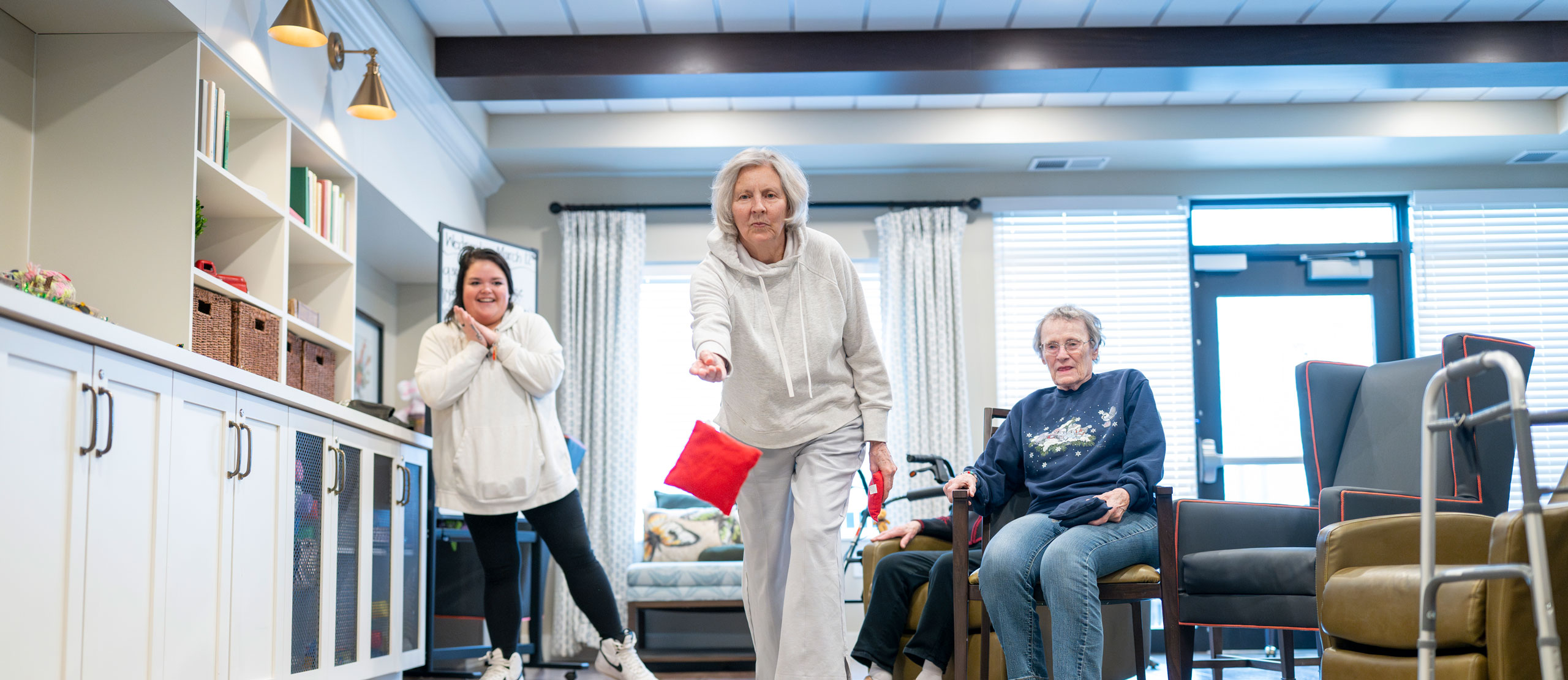 Memory Care residents play bean bag toss in the living room.