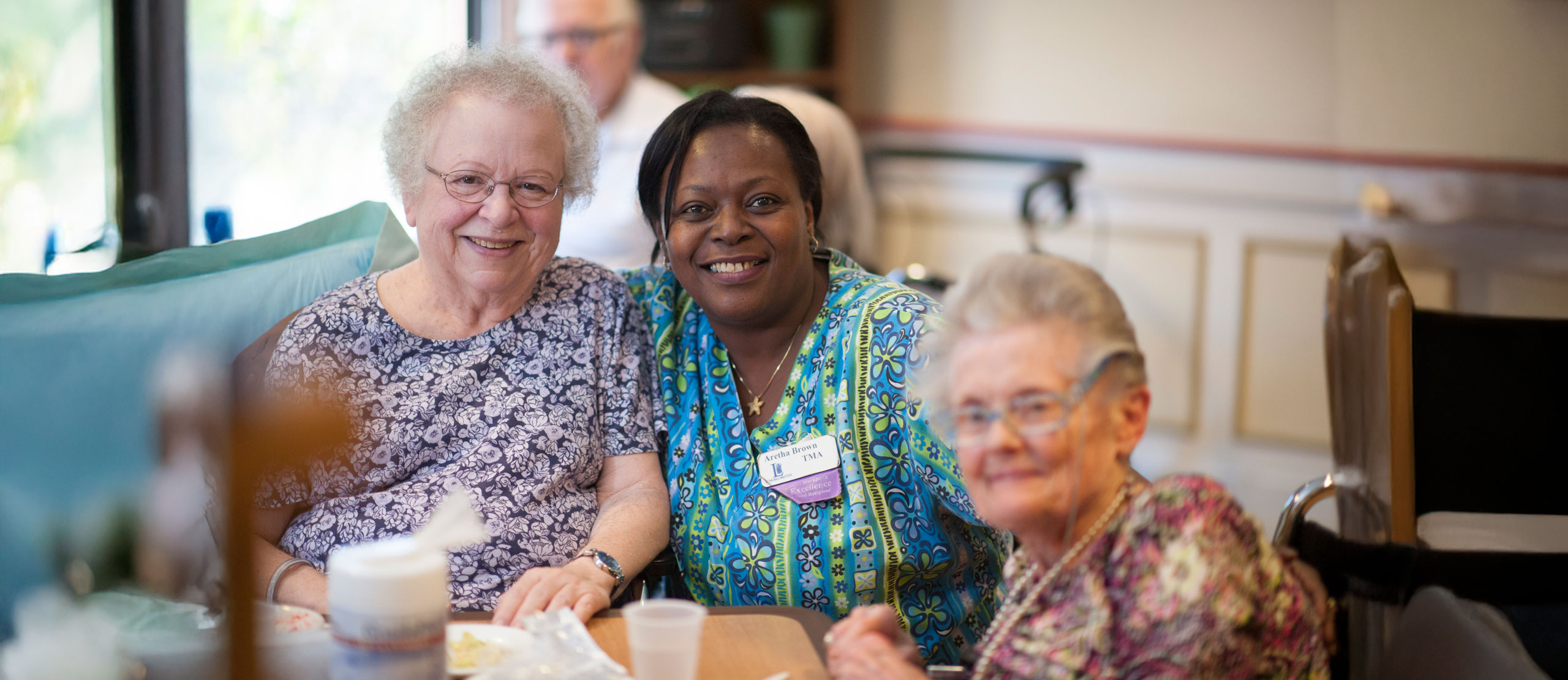 A care center employee warmly embracing a resident as they both smiled for the camera.