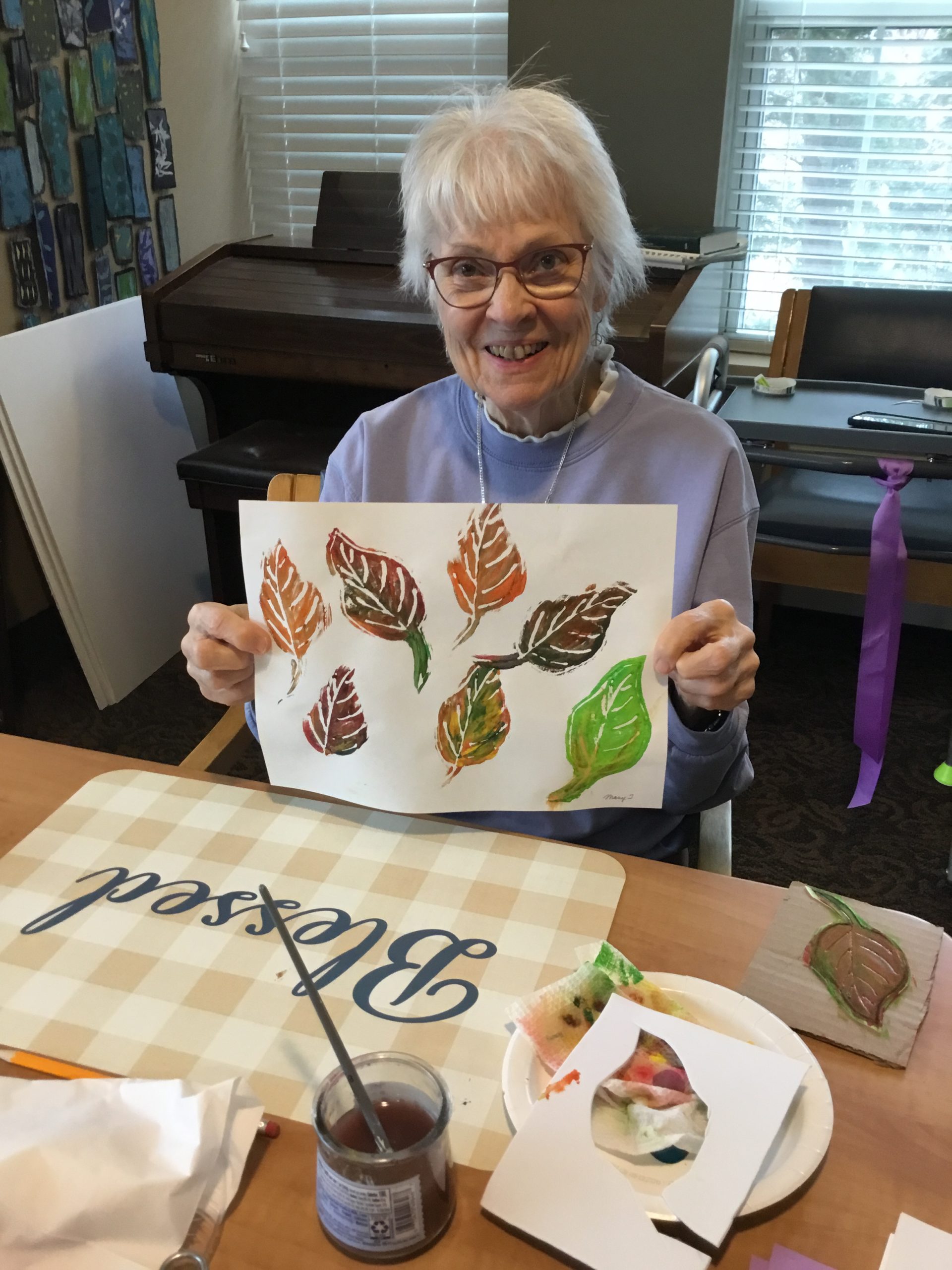 A resident from The Heritage at Lyngblomsten holds up her paper of fall colored leaves while participating in Art with Heart.