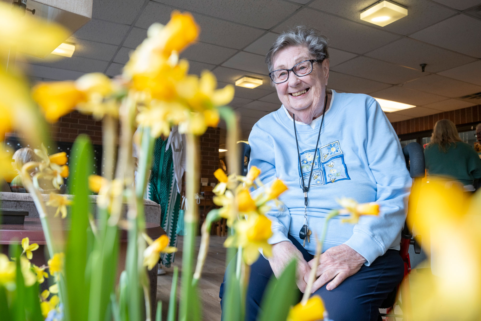 A Lady from the Lyngblomsten Apartments Smiles Brightly into the Camera with Beautiful Yellow Flowers in the Foreground