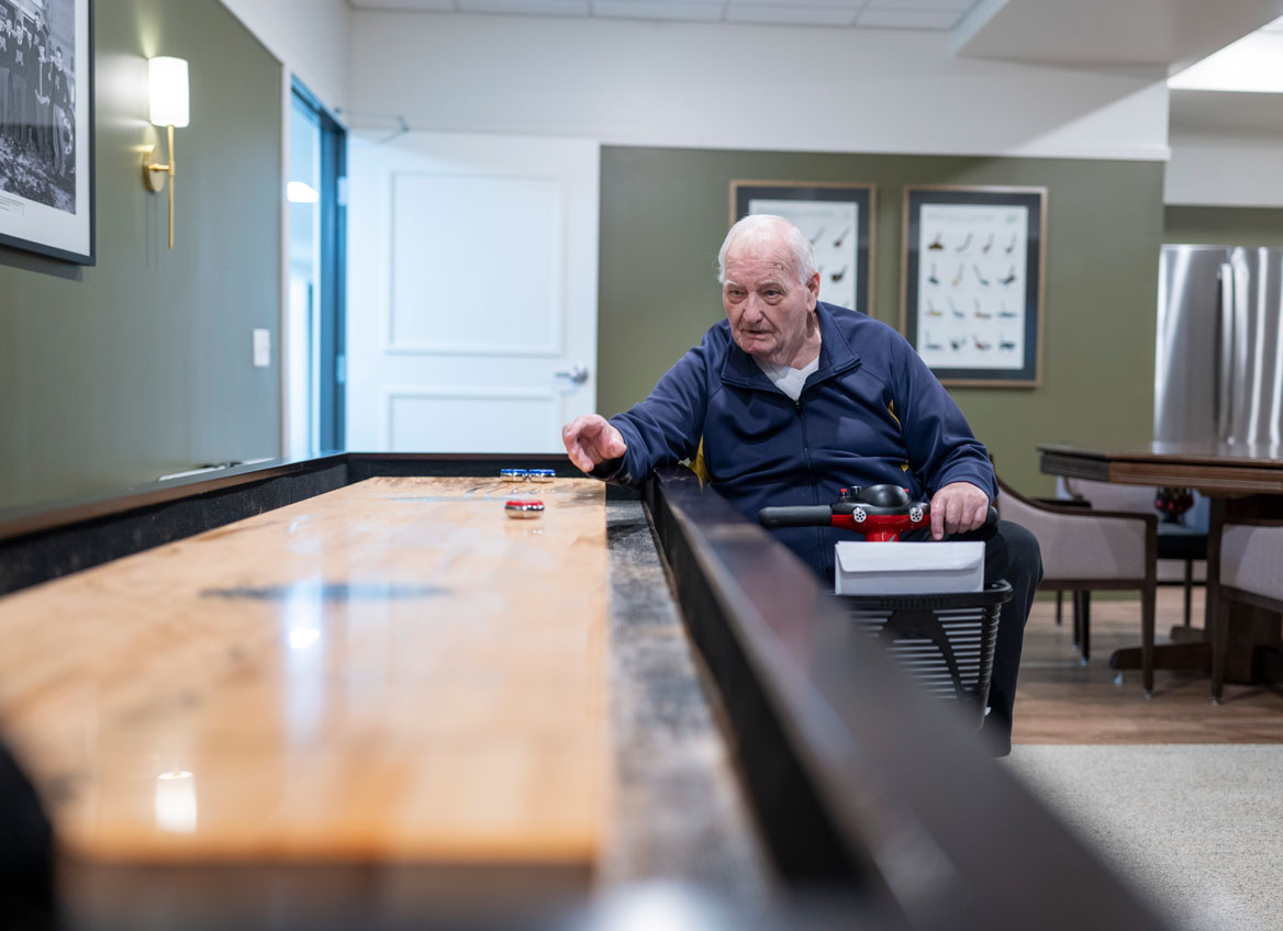 A Resident in a Wheelchair is Focused as he Plays Shuffleboard